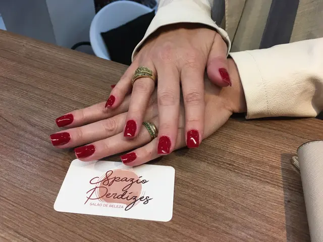 Mãos com unhas vermelhas sobre a mesa, ao lado do cartão do Spazio Perdizes